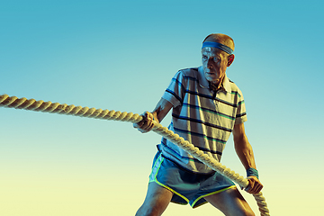 Image showing Senior man training with ropes in sportwear on gradient background and neon light