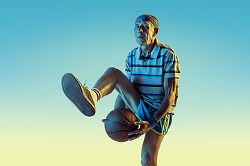 Image showing Senior man playing basketball in sportwear on gradient background and neon light