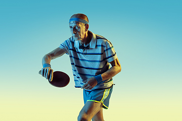 Image showing Senior man playing table tennis in sportwear on gradient background and neon light