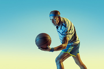 Image showing Senior man playing basketball in sportwear on gradient background and neon light