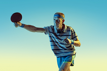 Image showing Senior man playing table tennis in sportwear on gradient background and neon light