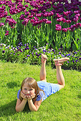 Image showing little girl lies on the grass near the tulips