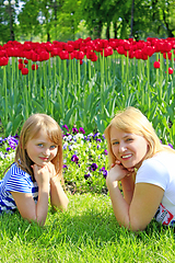 Image showing little girl and her mother lay on the grass near the tulips