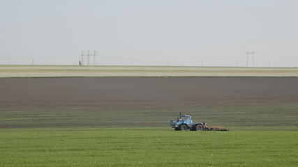 Image showing Blue wheeled tractor plowing a green field