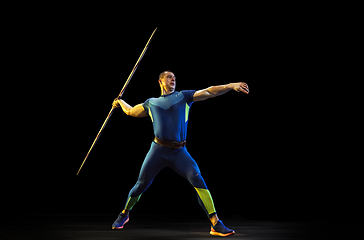 Image showing Male athlete practicing in throwing javelin isolated on black studio background in neon light