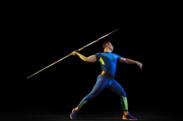 Image showing Male athlete practicing in throwing javelin isolated on black studio background in neon light