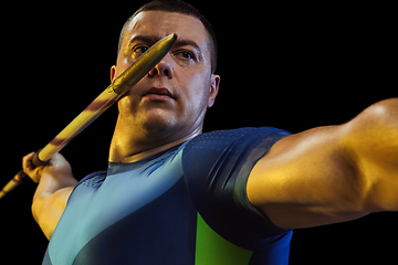 Image showing Male athlete practicing in throwing javelin isolated on black studio background in neon light