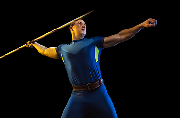 Image showing Male athlete practicing in throwing javelin isolated on black studio background in neon light