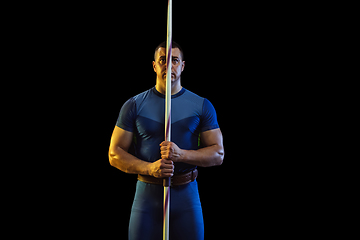 Image showing Male athlete practicing in throwing javelin isolated on black studio background in neon light