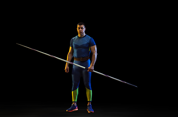 Image showing Male athlete practicing in throwing javelin isolated on black studio background in neon light