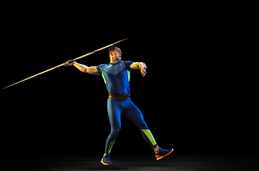 Image showing Male athlete practicing in throwing javelin isolated on black studio background in neon light