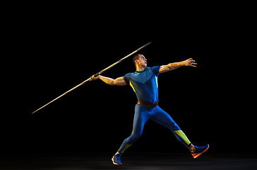 Image showing Male athlete practicing in throwing javelin isolated on black studio background in neon light