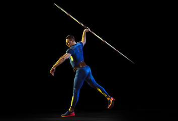 Image showing Male athlete practicing in throwing javelin isolated on black studio background in neon light