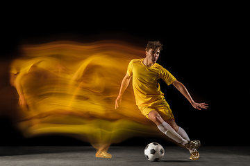 Image showing Young caucasian male football or soccer player kicking ball for the goal in mixed light on dark background. Concept of healthy lifestyle, professional sport, hobby.