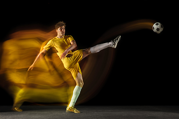 Image showing Young caucasian male football or soccer player kicking ball for the goal in mixed light on dark background. Concept of healthy lifestyle, professional sport, hobby.