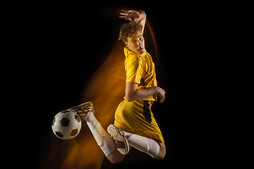 Image showing Young caucasian male football or soccer player kicking ball for the goal in mixed light on dark background. Concept of healthy lifestyle, professional sport, hobby.