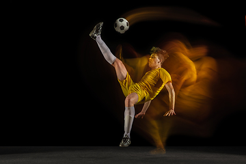 Image showing Young caucasian male football or soccer player kicking ball for the goal in mixed light on dark background. Concept of healthy lifestyle, professional sport, hobby.