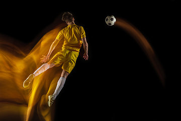 Image showing Young caucasian male football or soccer player kicking ball for the goal in mixed light on dark background. Concept of healthy lifestyle, professional sport, hobby.