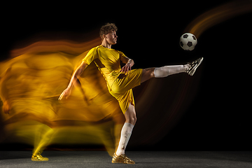 Image showing Young caucasian male football or soccer player kicking ball for the goal in mixed light on dark background. Concept of healthy lifestyle, professional sport, hobby.