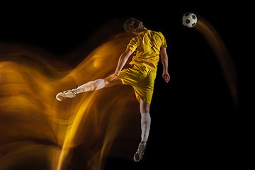 Image showing Young caucasian male football or soccer player kicking ball for the goal in mixed light on dark background. Concept of healthy lifestyle, professional sport, hobby.