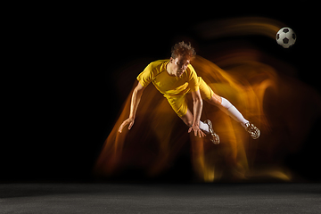 Image showing Young caucasian male football or soccer player kicking ball for the goal in mixed light on dark background. Concept of healthy lifestyle, professional sport, hobby.