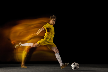 Image showing Young caucasian male football or soccer player kicking ball for the goal in mixed light on dark background. Concept of healthy lifestyle, professional sport, hobby.