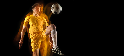 Image showing Young caucasian male football or soccer player kicking ball for the goal in mixed light on dark background. Concept of healthy lifestyle, professional sport, hobby.