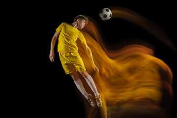 Image showing Young caucasian male football or soccer player kicking ball for the goal in mixed light on dark background. Concept of healthy lifestyle, professional sport, hobby.