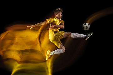 Image showing Young caucasian male football or soccer player kicking ball for the goal in mixed light on dark background. Concept of healthy lifestyle, professional sport, hobby.