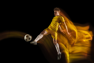 Image showing Young caucasian male football or soccer player kicking ball for the goal in mixed light on dark background. Concept of healthy lifestyle, professional sport, hobby.