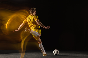 Image showing Young caucasian male football or soccer player kicking ball for the goal in mixed light on dark background. Concept of healthy lifestyle, professional sport, hobby.