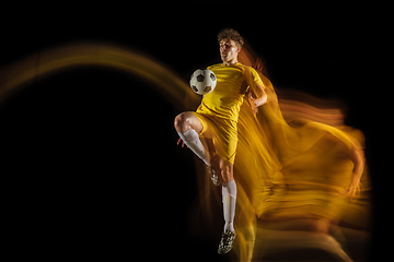 Image showing Young caucasian male football or soccer player kicking ball for the goal in mixed light on dark background. Concept of healthy lifestyle, professional sport, hobby.