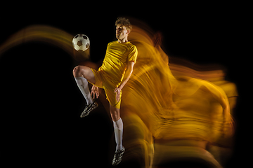 Image showing Young caucasian male football or soccer player kicking ball for the goal in mixed light on dark background. Concept of healthy lifestyle, professional sport, hobby.