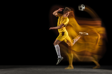 Image showing Young caucasian male football or soccer player kicking ball for the goal in mixed light on dark background. Concept of healthy lifestyle, professional sport, hobby.