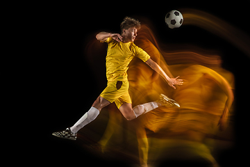 Image showing Young caucasian male football or soccer player kicking ball for the goal in mixed light on dark background. Concept of healthy lifestyle, professional sport, hobby.