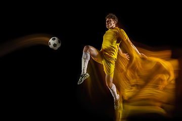 Image showing Young caucasian male football or soccer player kicking ball for the goal in mixed light on dark background. Concept of healthy lifestyle, professional sport, hobby.