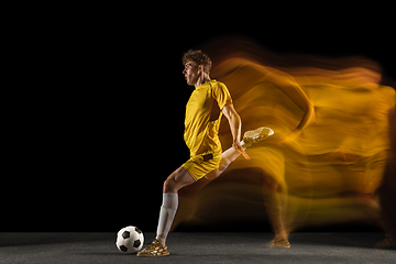 Image showing Young caucasian male football or soccer player kicking ball for the goal in mixed light on dark background. Concept of healthy lifestyle, professional sport, hobby.