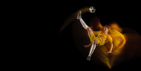 Image showing Young caucasian male football or soccer player kicking ball for the goal in mixed light on dark background. Concept of healthy lifestyle, professional sport, hobby.