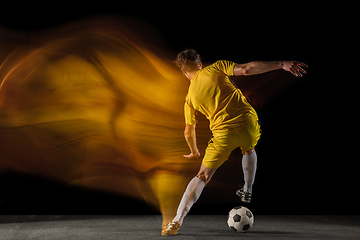 Image showing Young caucasian male football or soccer player kicking ball for the goal in mixed light on dark background. Concept of healthy lifestyle, professional sport, hobby.