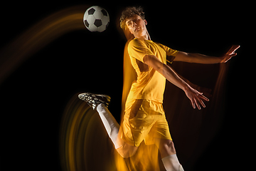 Image showing Young caucasian male football or soccer player kicking ball for the goal in mixed light on dark background. Concept of healthy lifestyle, professional sport, hobby.