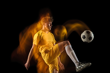 Image showing Young caucasian male football or soccer player kicking ball for the goal in mixed light on dark background. Concept of healthy lifestyle, professional sport, hobby.