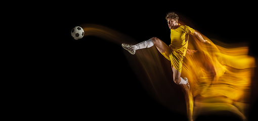 Image showing Young caucasian male football or soccer player kicking ball for the goal in mixed light on dark background. Concept of healthy lifestyle, professional sport, hobby.