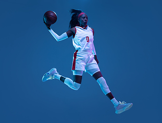 Image showing Beautiful african-american female basketball player in motion and action in neon light on blue background. Concept of healthy lifestyle, professional sport, hobby.