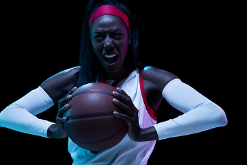 Image showing Beautiful african-american female basketball player in motion and action in neon light on black background. Concept of healthy lifestyle, professional sport, hobby.