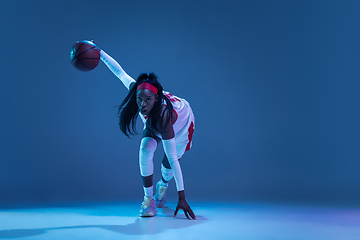 Image showing Beautiful african-american female basketball player in motion and action in neon light on blue background. Concept of healthy lifestyle, professional sport, hobby.