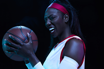 Image showing Beautiful african-american female basketball player in motion and action in neon light on black background. Concept of healthy lifestyle, professional sport, hobby.