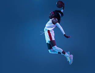 Image showing Beautiful african-american female basketball player in motion and action in neon light on blue background. Concept of healthy lifestyle, professional sport, hobby.