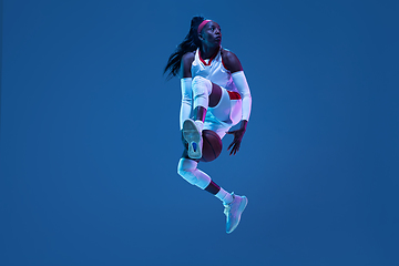 Image showing Beautiful african-american female basketball player in motion and action in neon light on blue background. Concept of healthy lifestyle, professional sport, hobby.