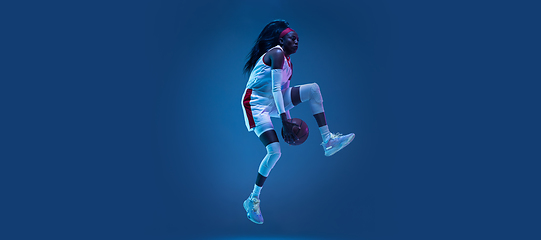 Image showing Beautiful african-american female basketball player in motion and action in neon light on blue background. Concept of healthy lifestyle, professional sport, hobby.