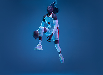 Image showing Beautiful african-american female basketball player in motion and action in neon light on blue background. Concept of healthy lifestyle, professional sport, hobby.